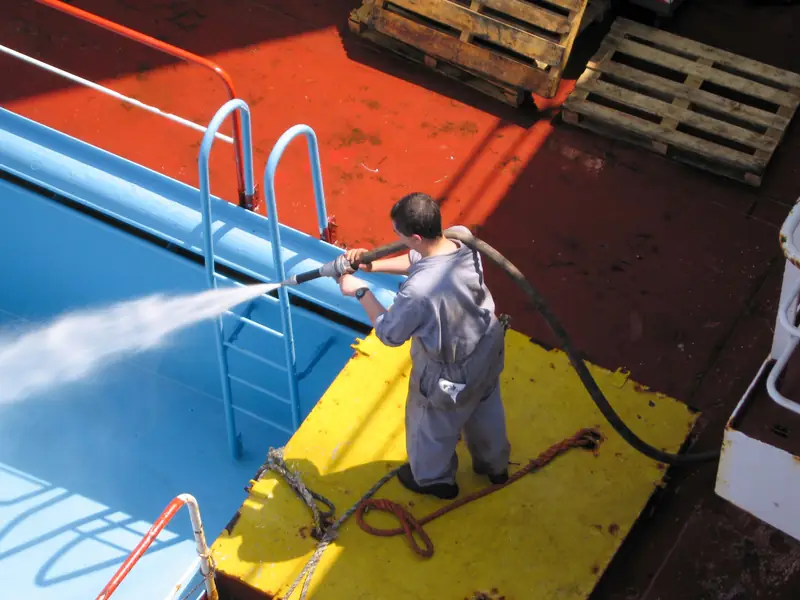 A worker cleaning a ship’s deck with a high pressure water jet