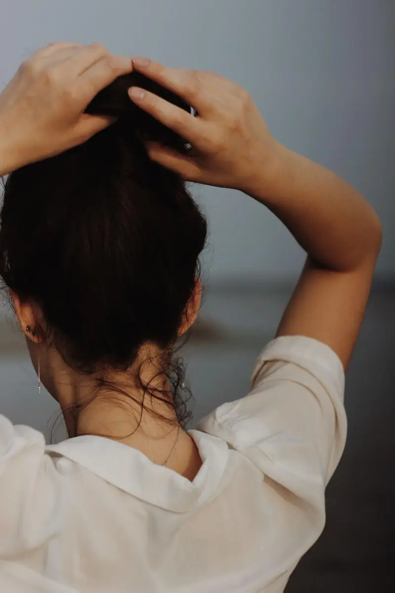 A woman with dark brunette hair gathering it into a bun, seen from behind